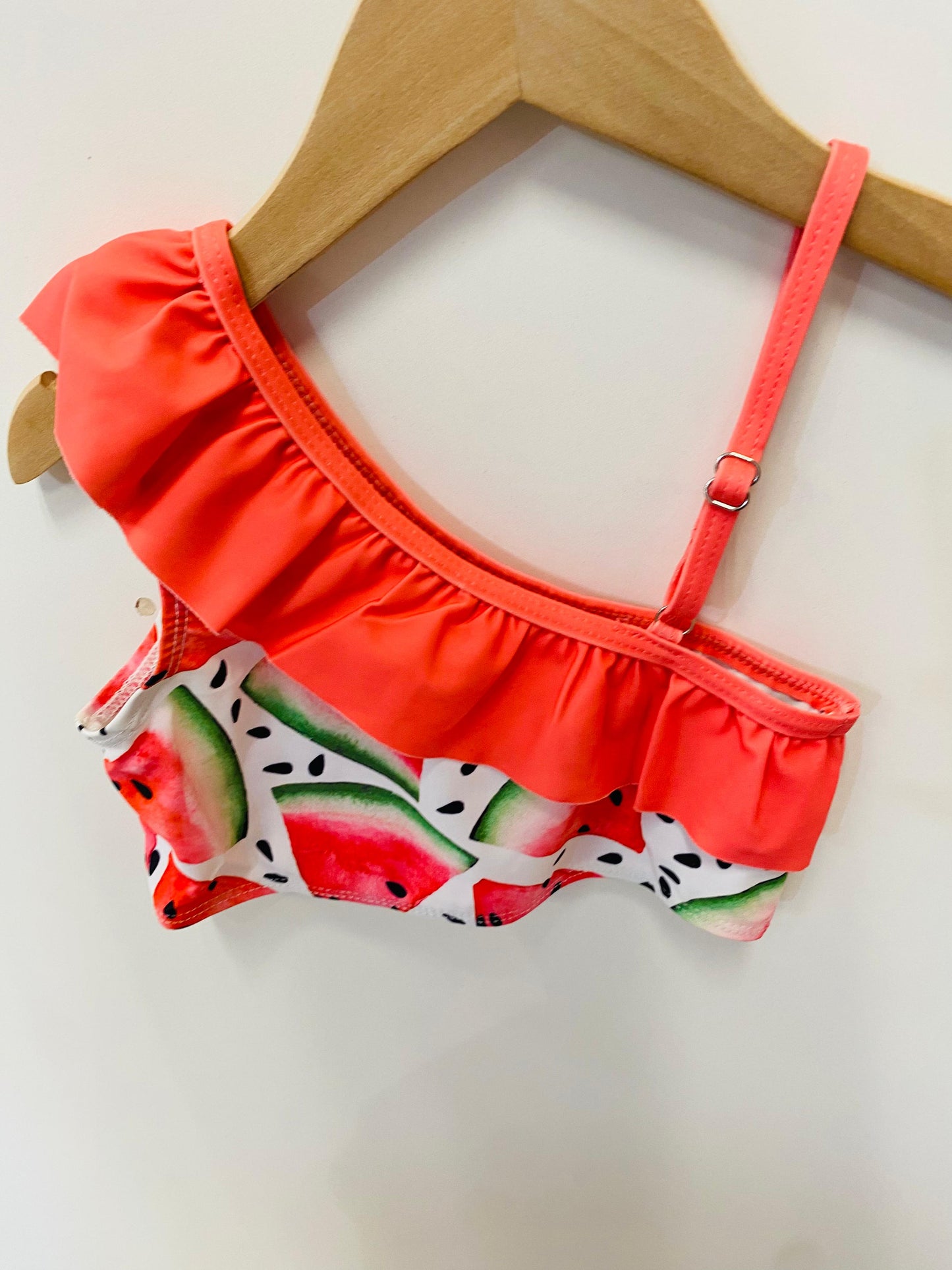 Red bikini top with watermelon pattern on a wooden hanger against a white background