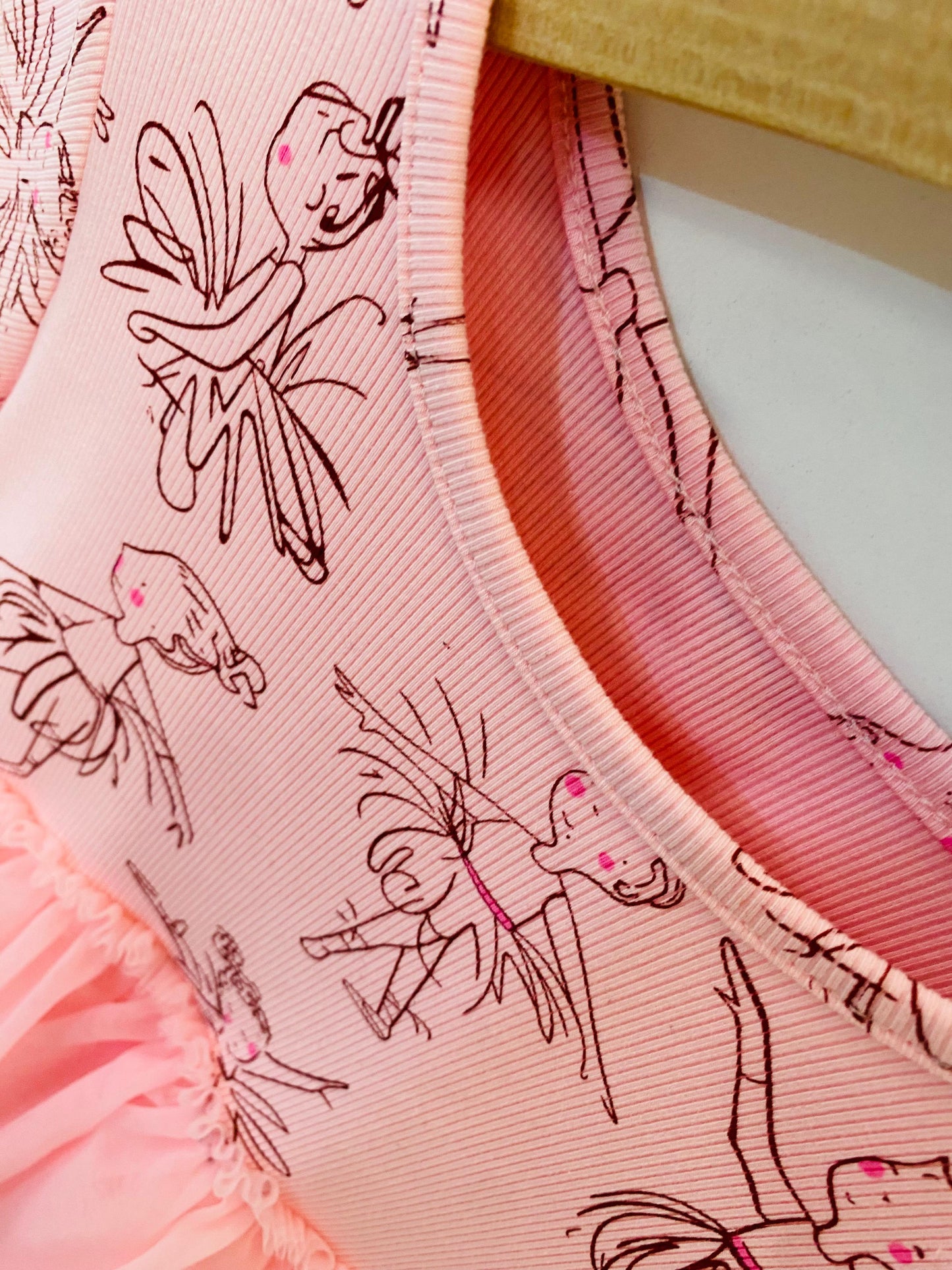 Close-up of a pink garment with fairy designs and ruffled hem.