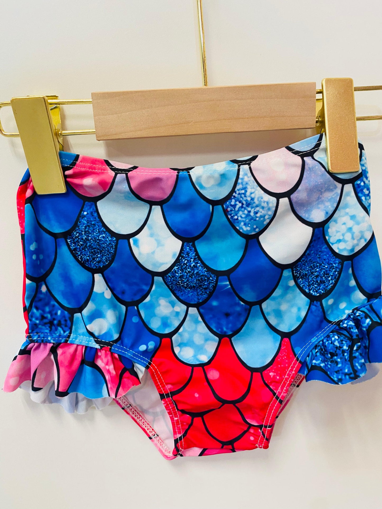 Colorful fish-scale patterned shorts on a hanger against a white background