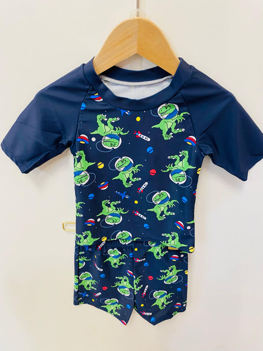 Navy blue swim shirt with green dinosaur pattern on a wooden hanger against a white background