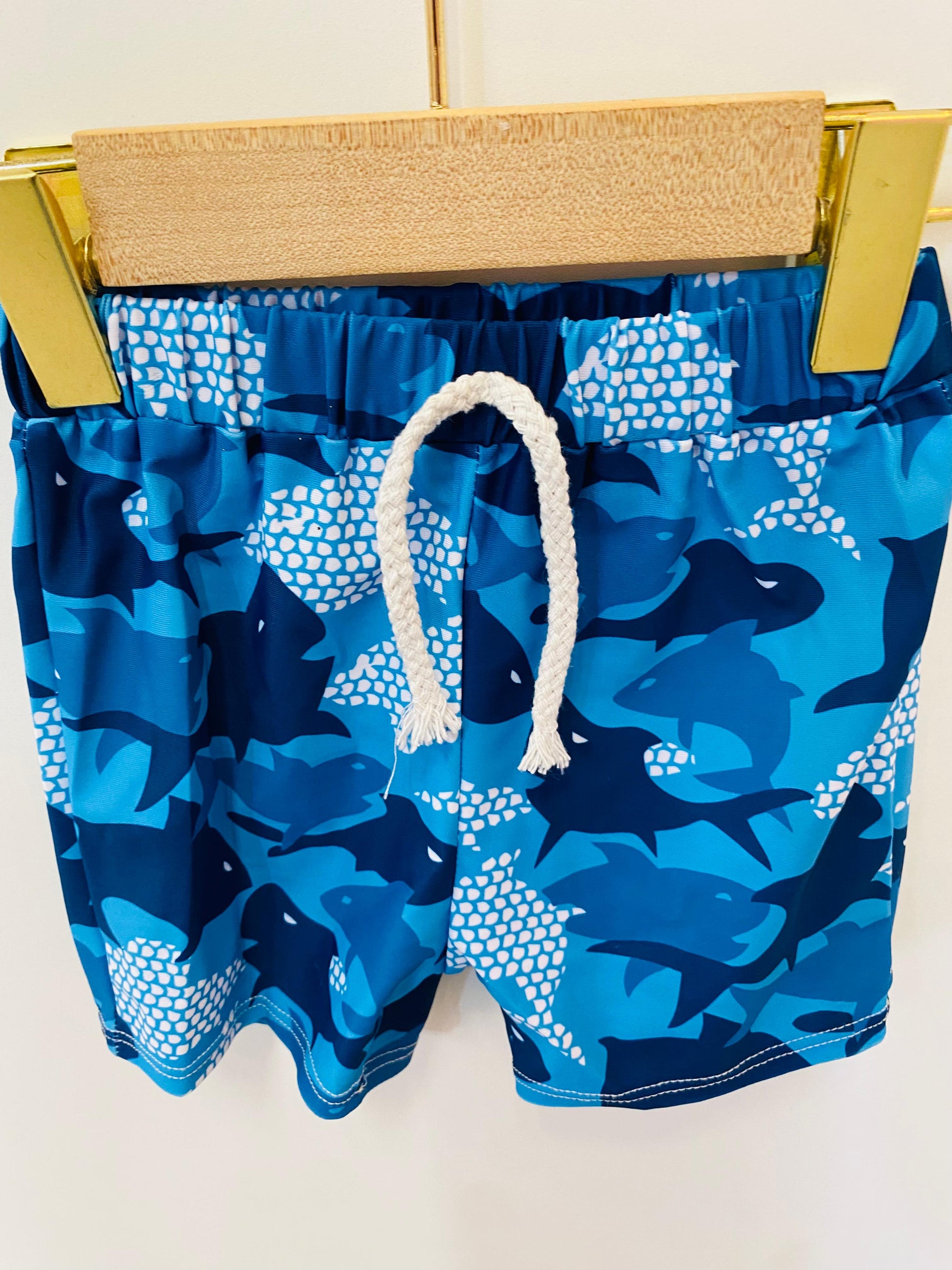 Blue swim shorts with shark pattern on a hanger against a white background