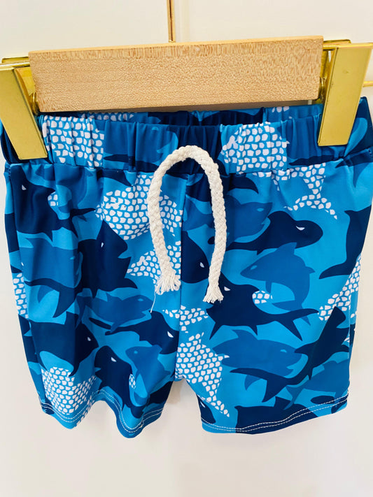 Blue swim shorts with shark pattern on a hanger against a white background