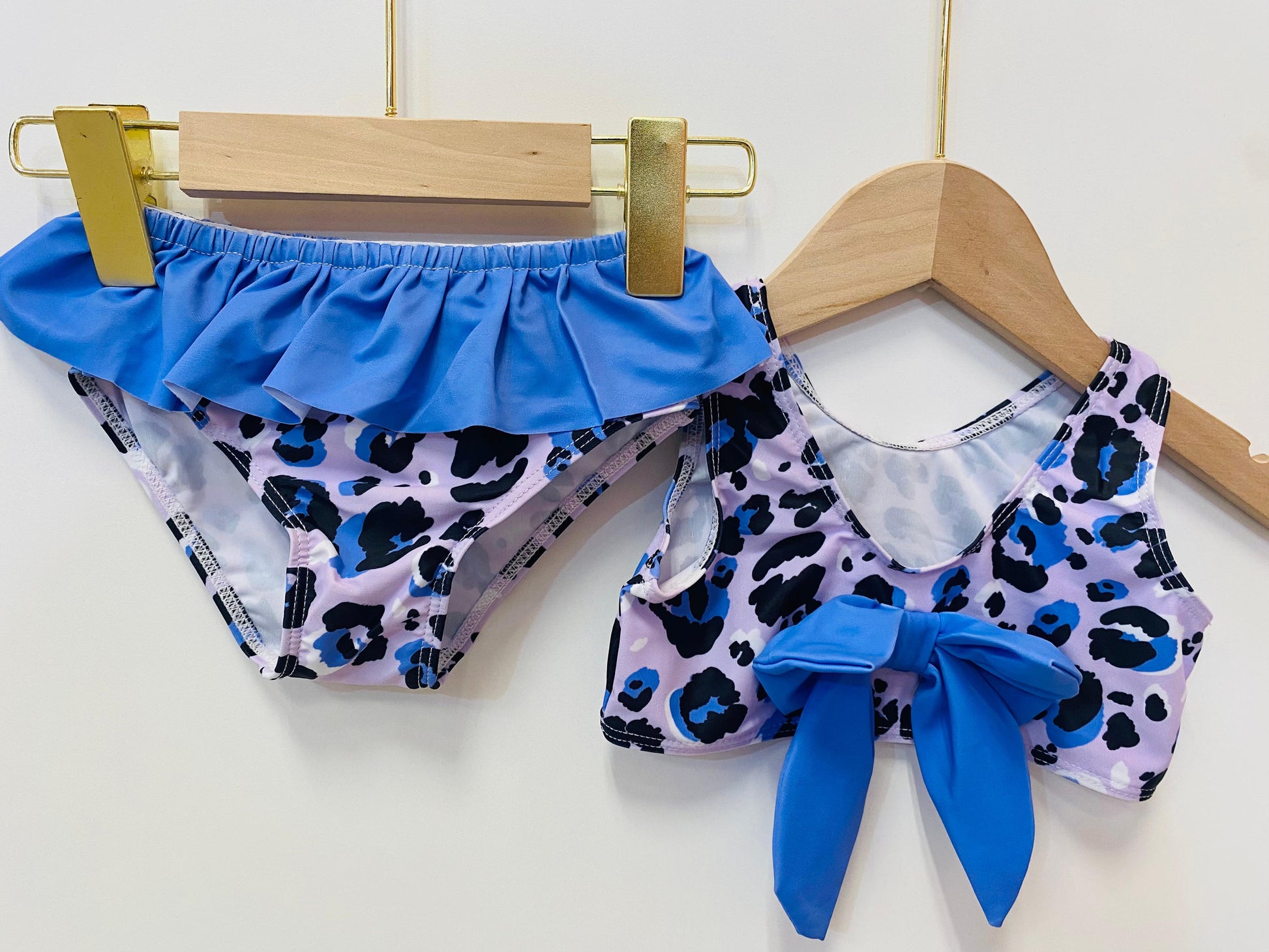 Children's swimsuit set with purple ruffled top and leopard print bottom on hangers.